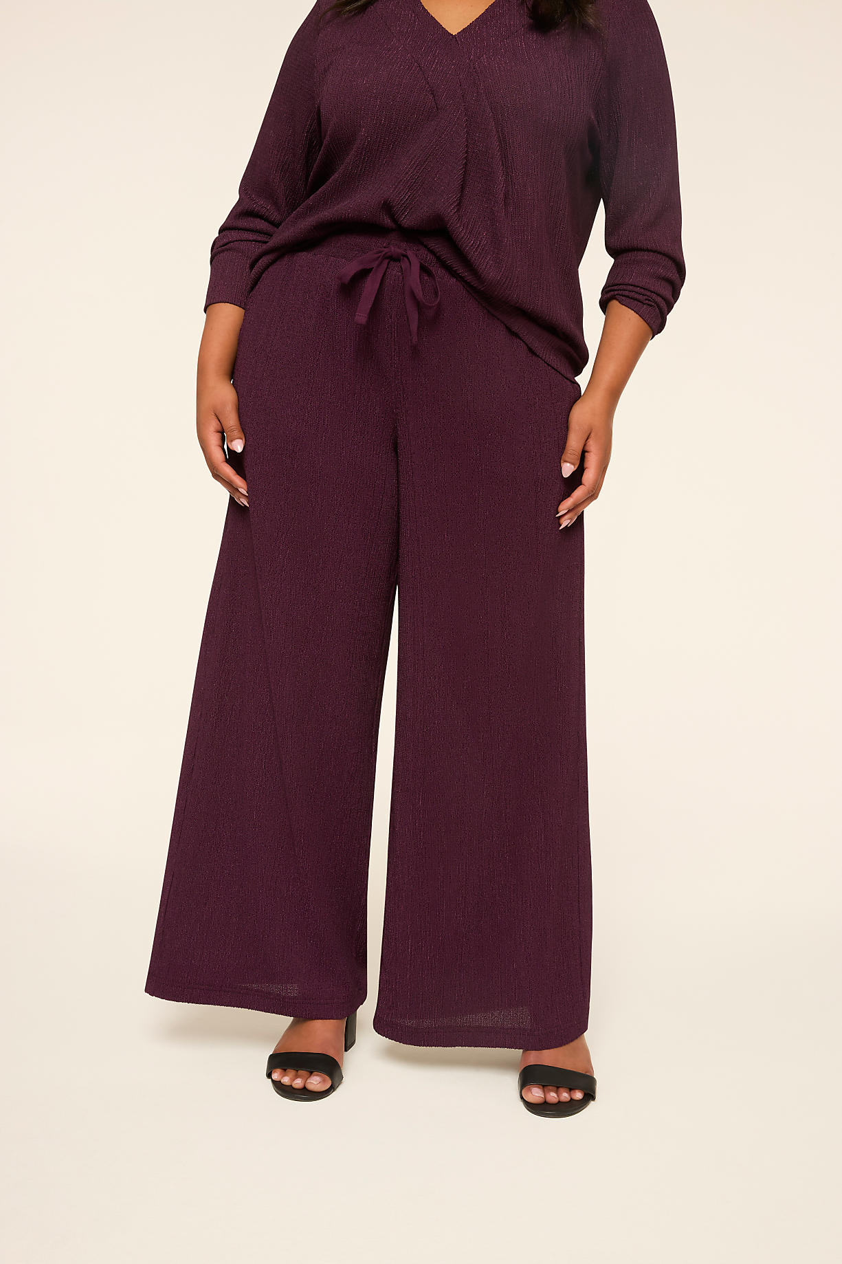 A person stands in the foreground wearing a plum-colored ribbed top and wide-leg pants, against a plain, light-colored background. Product Image 6