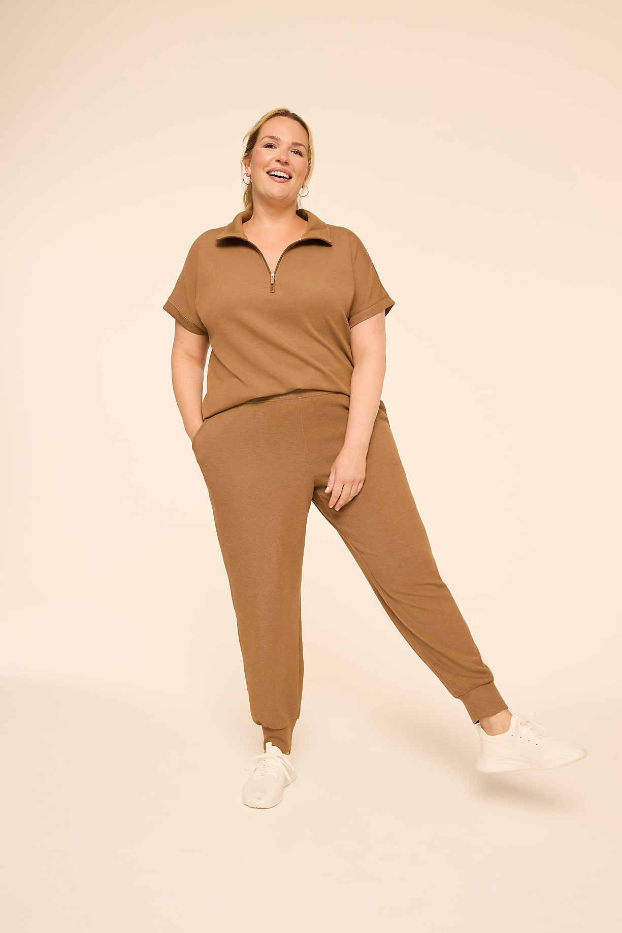 A smiling woman in a brown tracksuit stands with one leg extended against a plain, light-colored background. Product Image 4