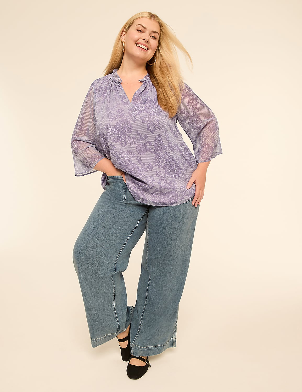 A smiling woman in a purple patterned blouse and wide-leg jeans poses against a plain, light-colored background. Product Image 4