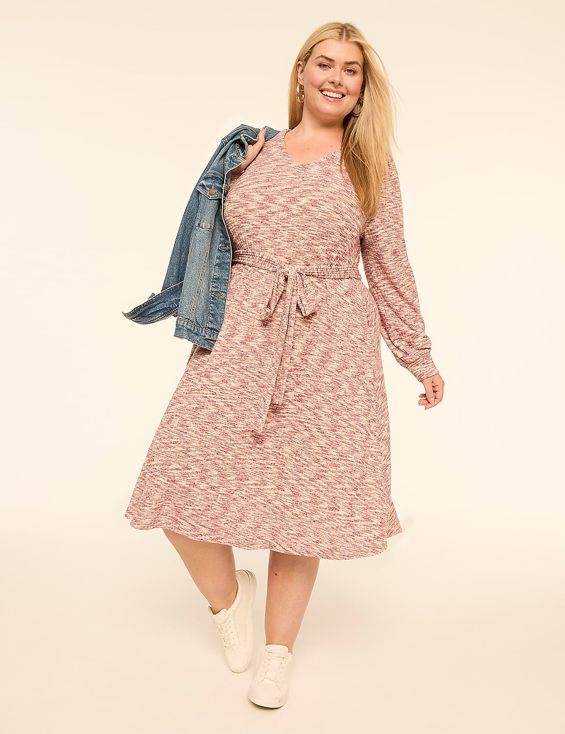 A smiling woman in a pink patterned dress and white sneakers, with a denim jacket slung over her shoulder, poses against a plain cream background. Product Image 1