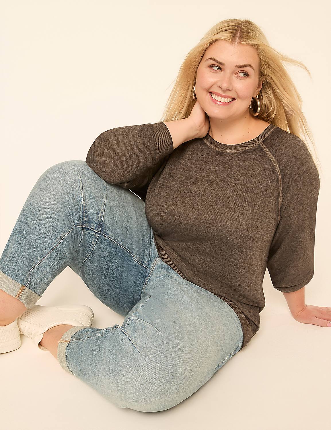A smiling woman with blonde hair, wearing a gray top and cuffed jeans, sits on a plain, light-colored background. Product Image 3