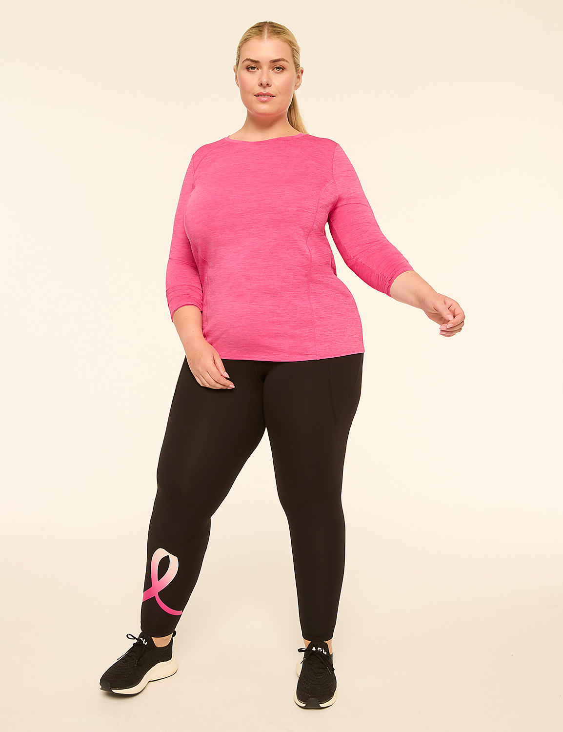 A woman in a pink top and black leggings with a pink ribbon design on the left leg stands against a plain cream background. Product Image 3
