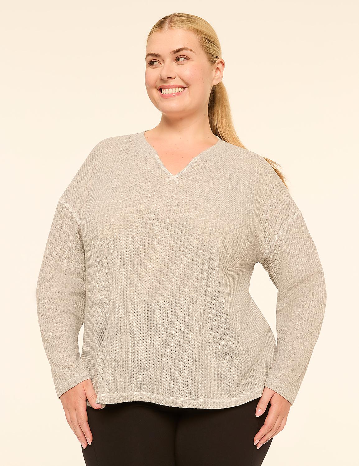 A smiling woman with blonde hair pulled back in a ponytail poses in a light gray, textured v-neck sweater and black pants against a plain, light beige background. Product Image 1