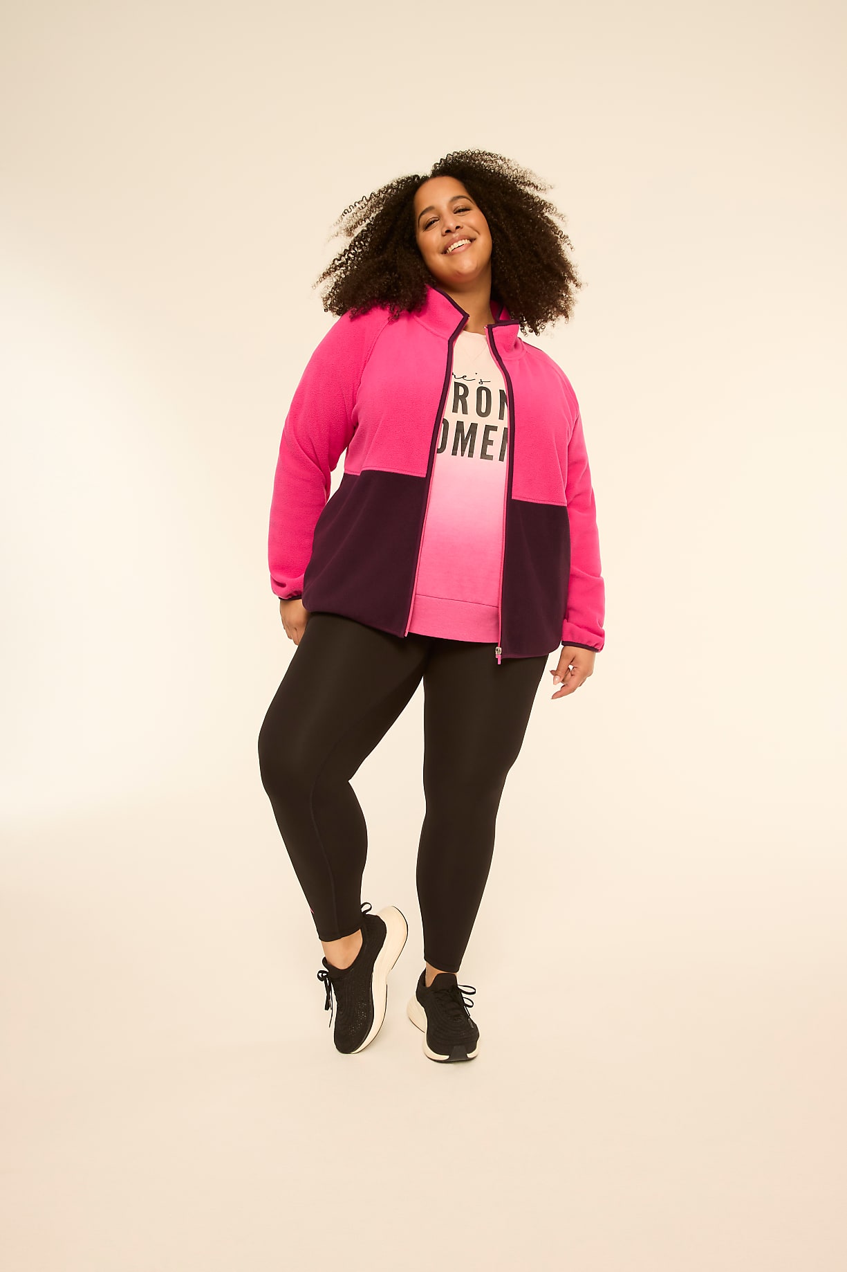 A smiling woman in a pink and purple jacket and black leggings stands against a plain, light-colored background. Product Image 5