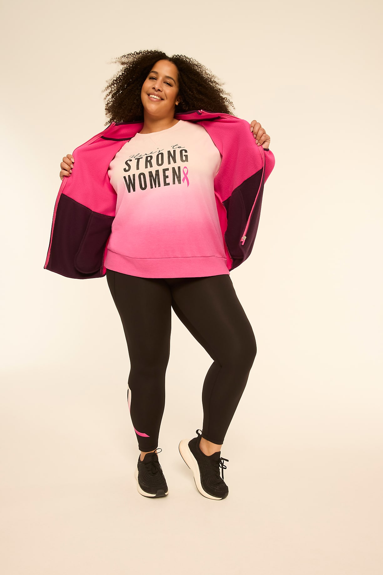 A smiling woman in a pink and purple jacket over a "STRONG WOMEN" sweatshirt and black leggings stands against a plain, light background. Product Image 7