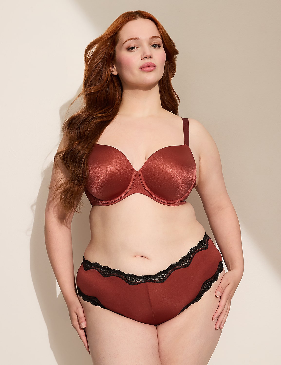 A woman with red hair poses in a rust-colored bra and underwear against a plain, softly lit background. Product Image 3