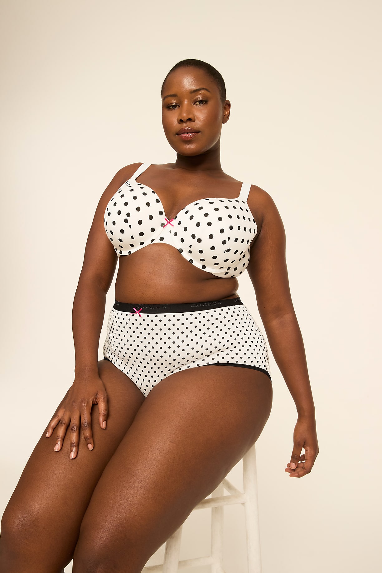 A woman in a polka dot bra and underwear sits on a stool against a plain background. Product Image 5