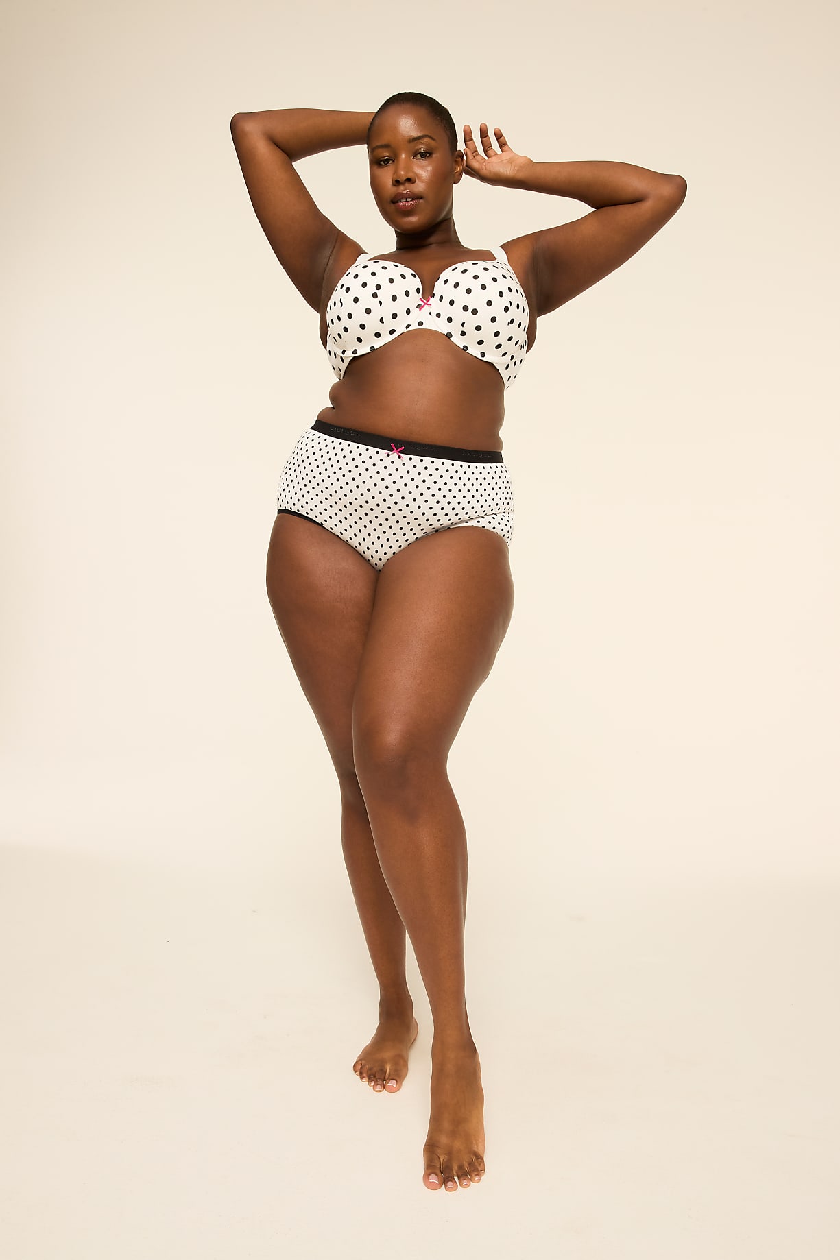 A woman in polka-dot lingerie poses with her hands behind her head against a plain, light-colored background. Product Image 8