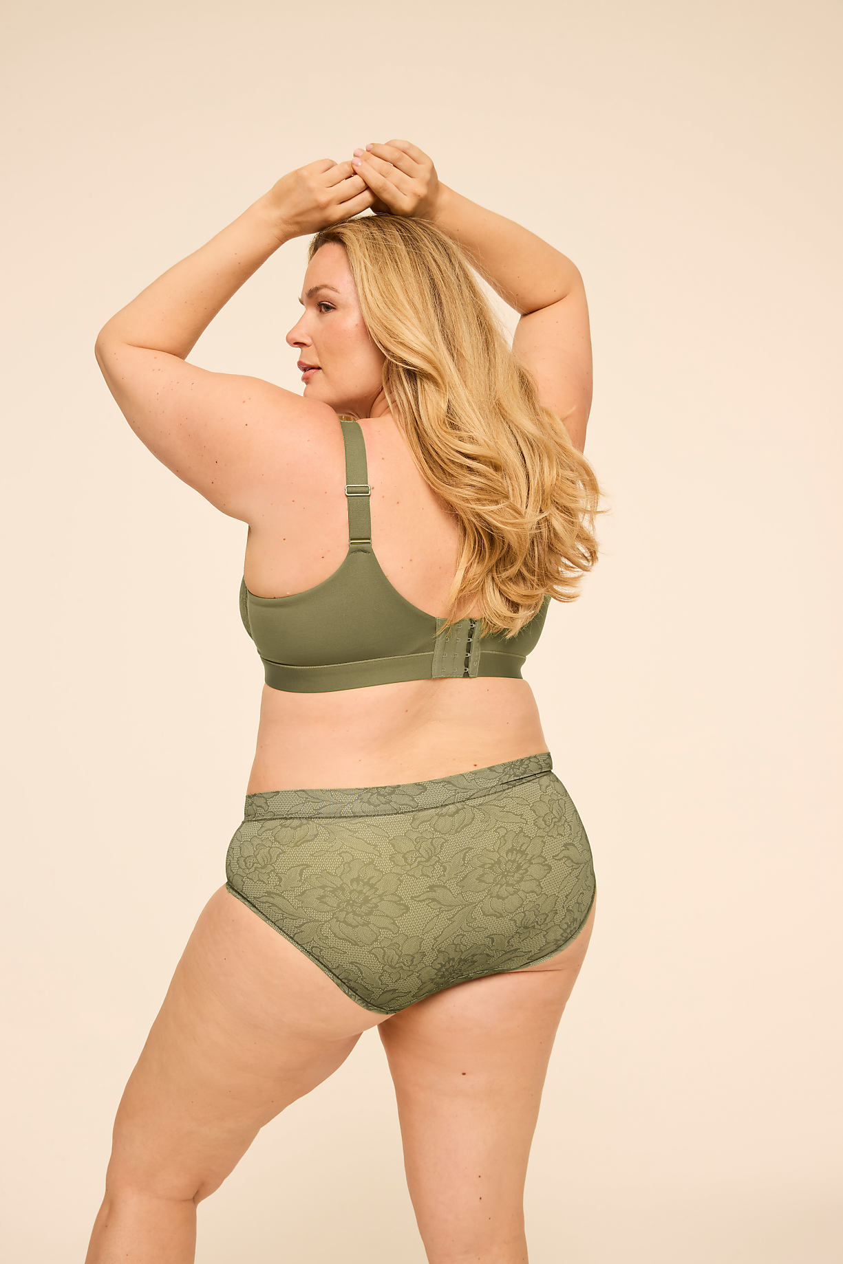 A woman in olive green lingerie poses with her arms raised against a plain, light beige background. Product Image 10