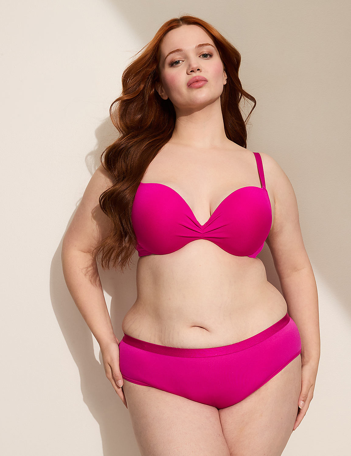 A woman with long, wavy red hair poses in a bright pink strapless bra and matching bottoms against a plain, light-colored wall with a shadow cast from the left. Product Image 2