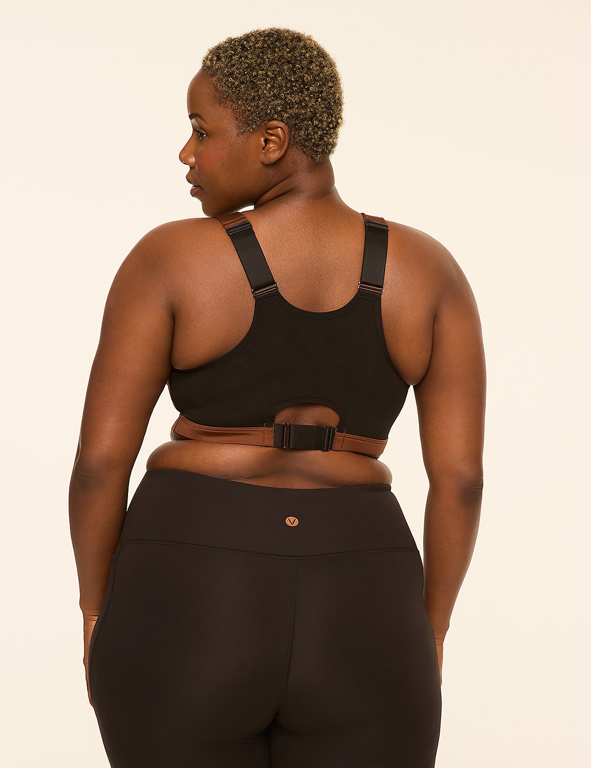 A woman with short, curly hair faces away from the camera, wearing a black sports bra and black leggings against a plain, light-colored background. Product Image 2