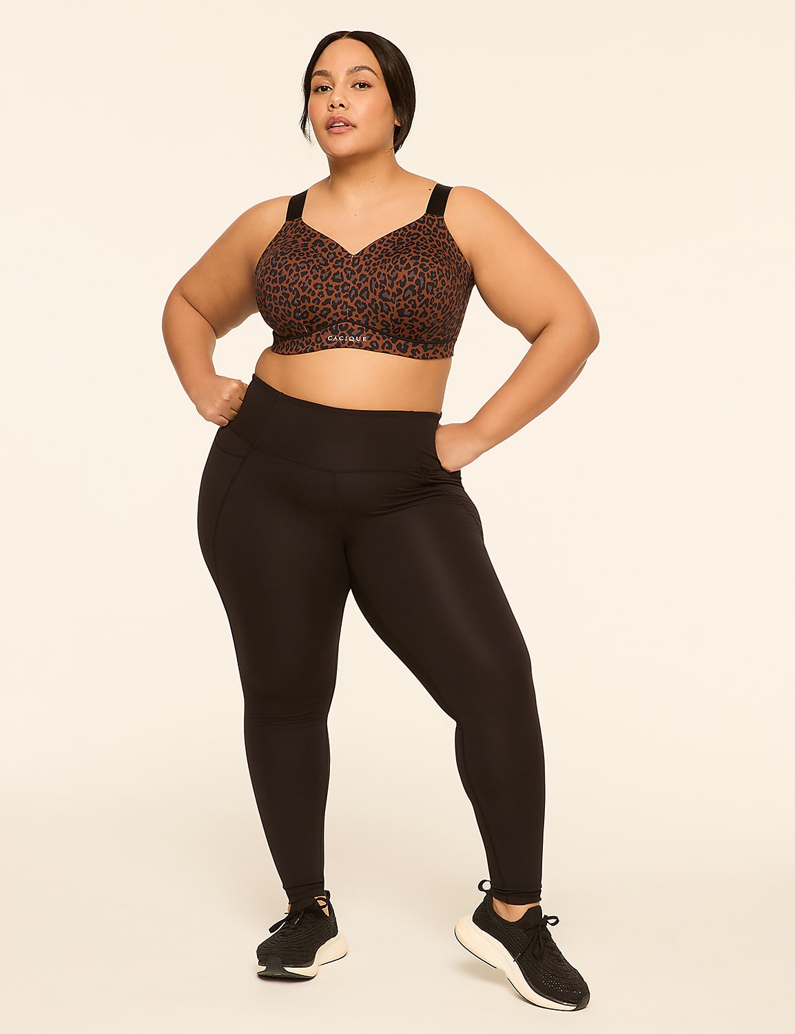 A woman in a leopard print sports bra and black leggings stands with her hands on her hips against a plain, light-colored background. Product Image 3