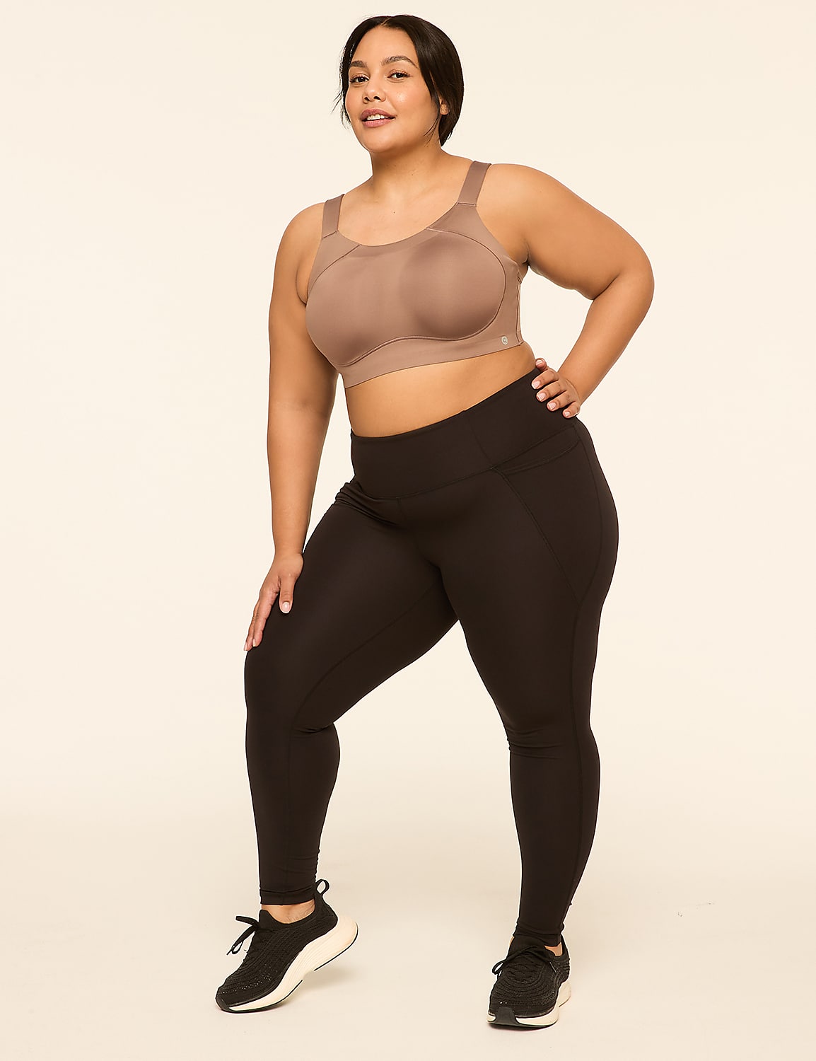 A woman in a taupe sports bra and black leggings stands with her hand on her hip against a plain, light-colored background. Product Image 3