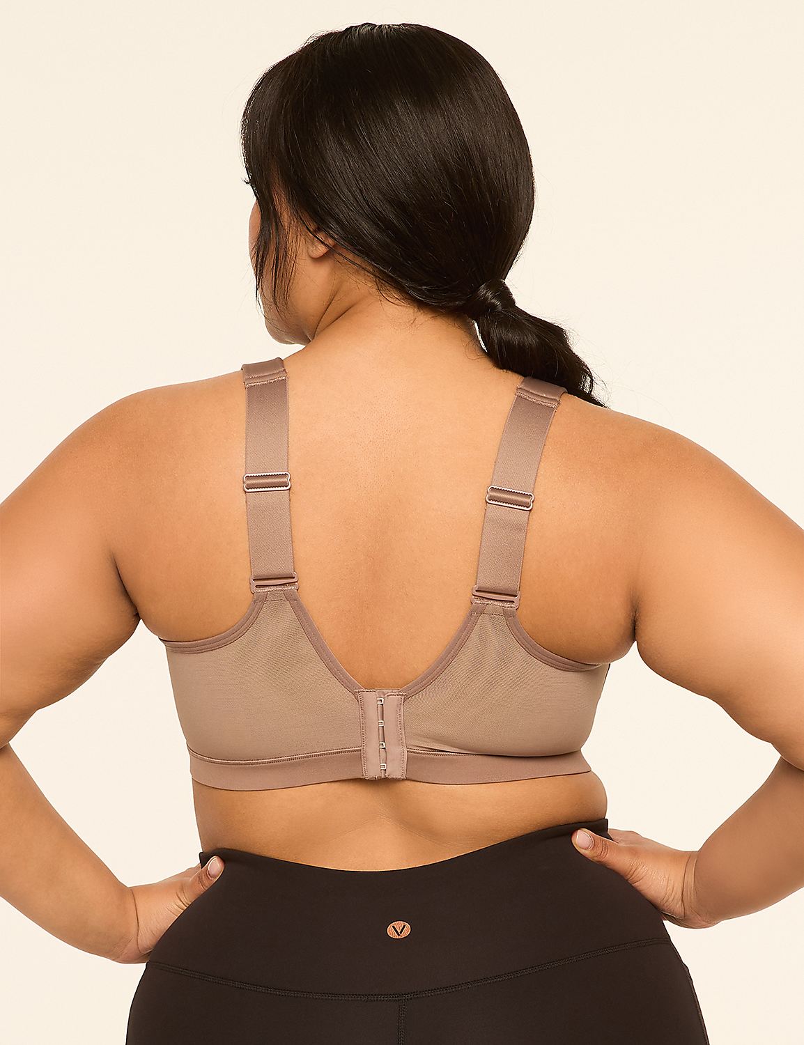 A woman with dark hair and a tan sports bra stands with her hands on her hips against a plain beige background. Product Image 2