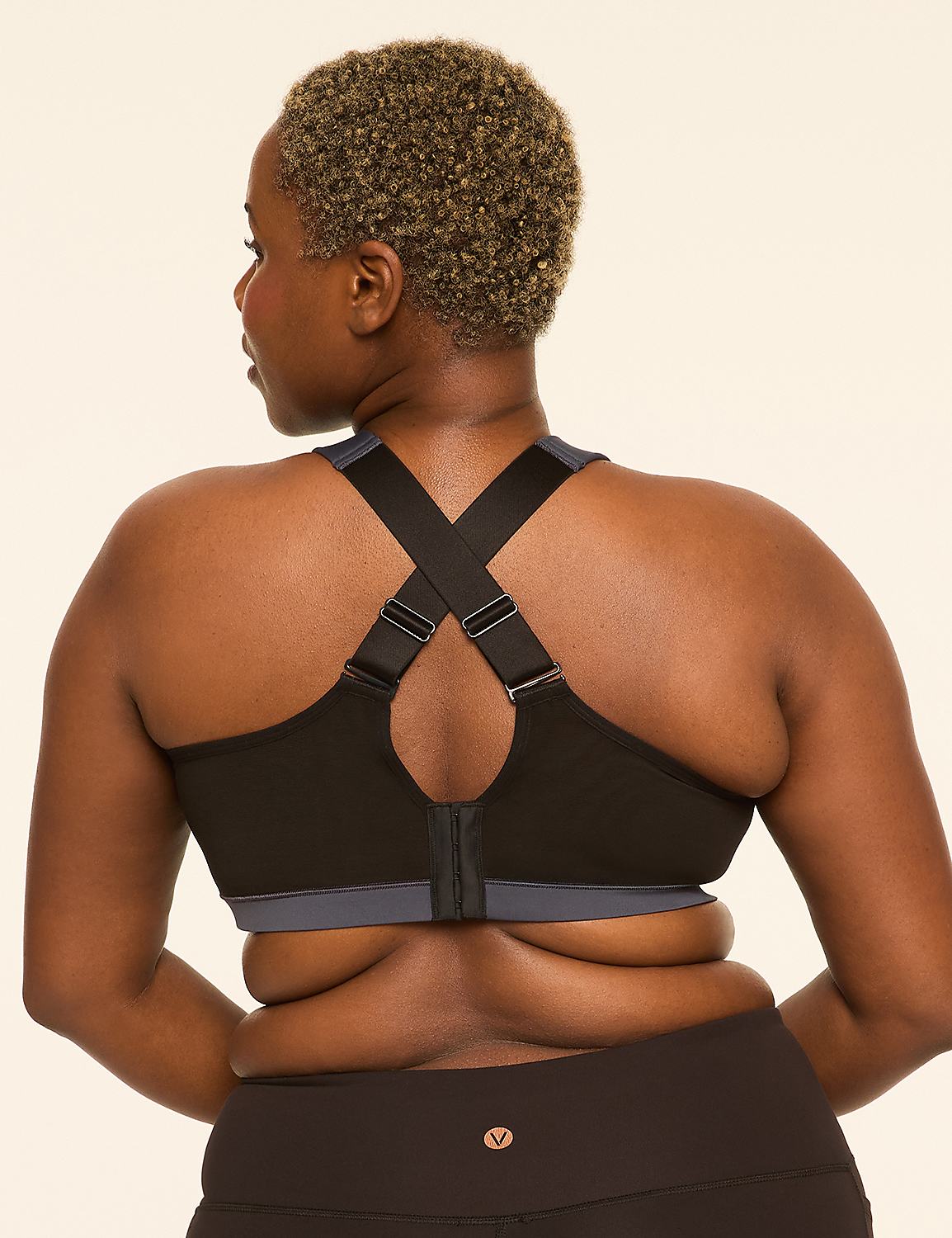 A woman with short, curly hair wears a black sports bra with gray trim, her back to the viewer, against a plain, light-colored background. Product Image 4