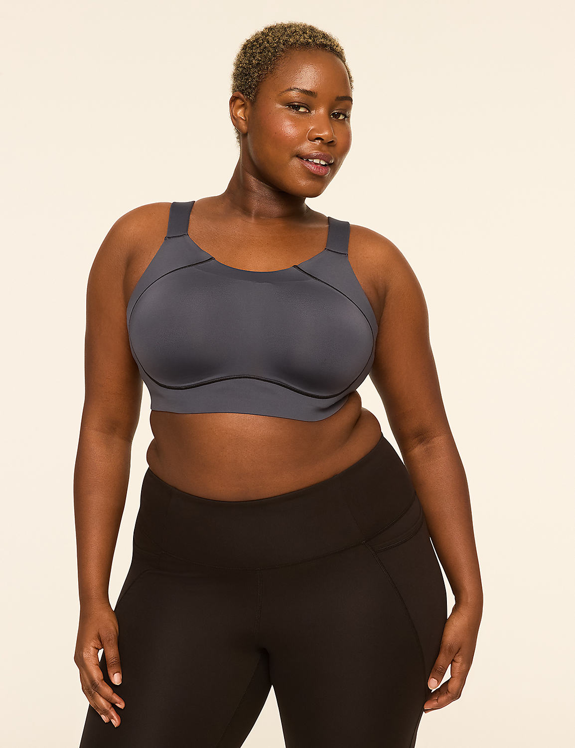 A woman with short, blonde hair and dark skin poses in a grey sports bra and black leggings against a plain, light-colored background. Product Image 1