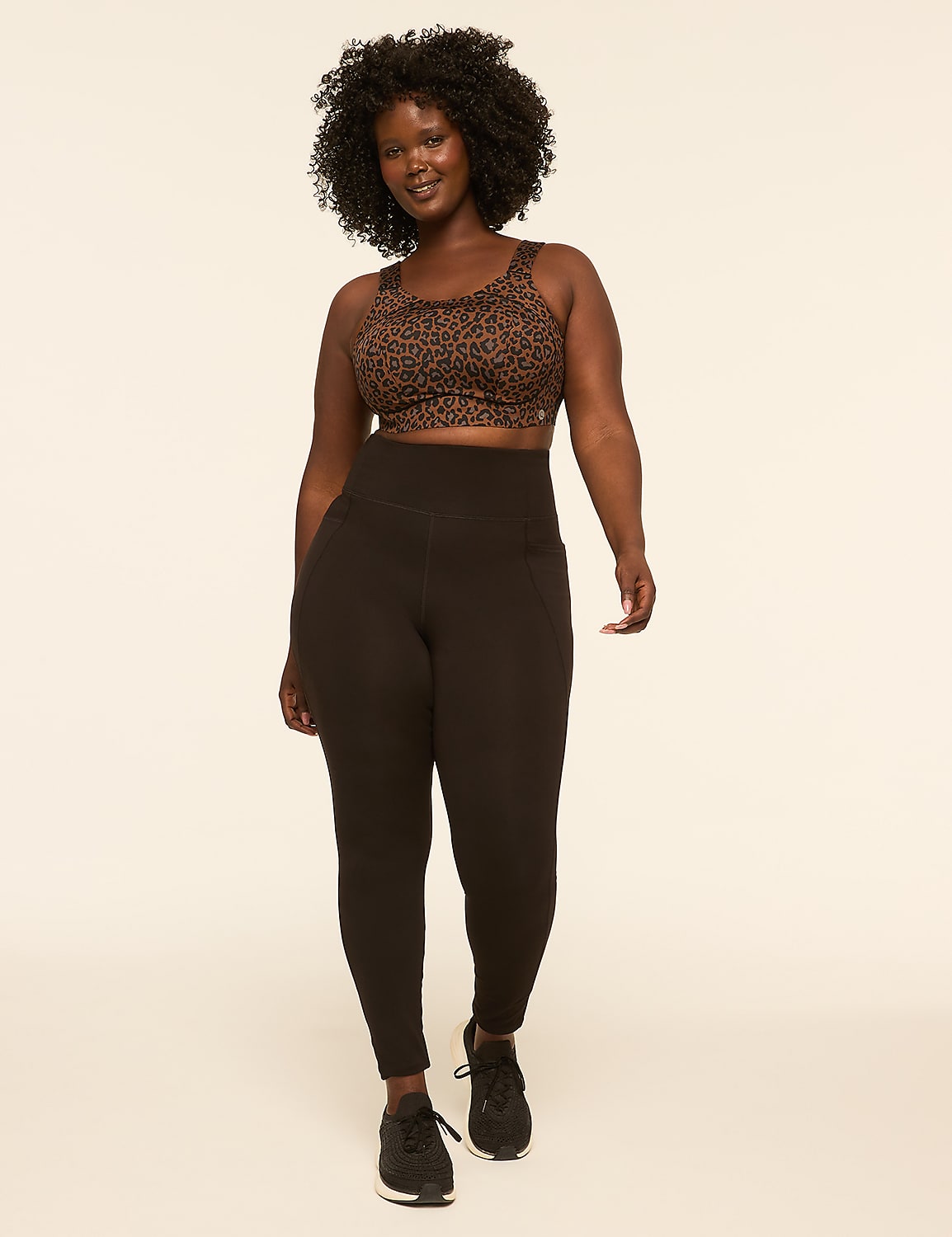 A woman with dark, curly hair and a leopard print sports bra and black leggings walks forward against a plain, light-colored background. Product Image 3