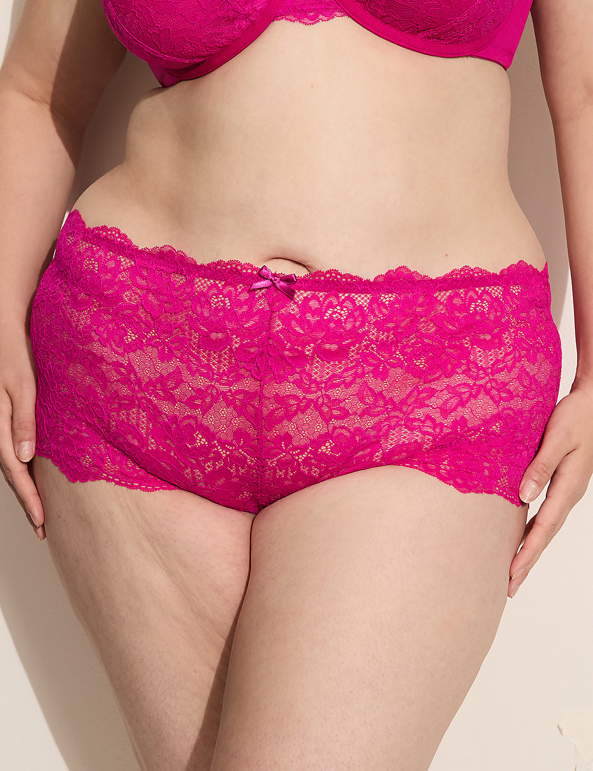 A person in bright pink lace underwear and bra stands against a plain, light-colored background. Product Image 1