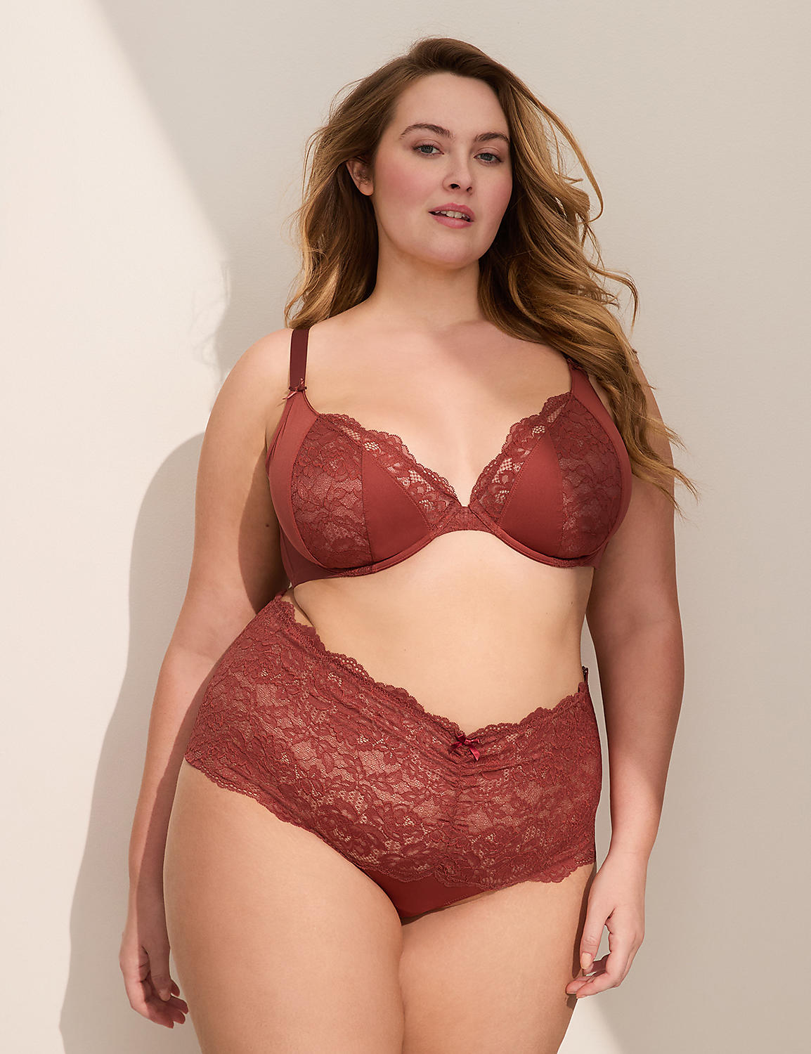 A woman in a rust-colored lace bra and matching high-waisted briefs stands against a plain, light-colored wall with soft shadows. Product Image 3