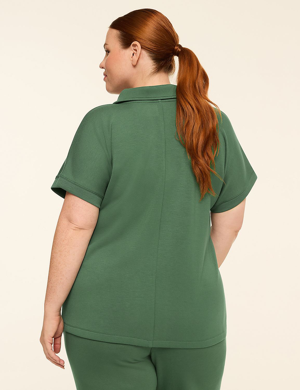 A woman with auburn hair pulled into a ponytail stands facing away from the camera, wearing a green polo shirt and pants against a plain, light-colored background. Product Image 2