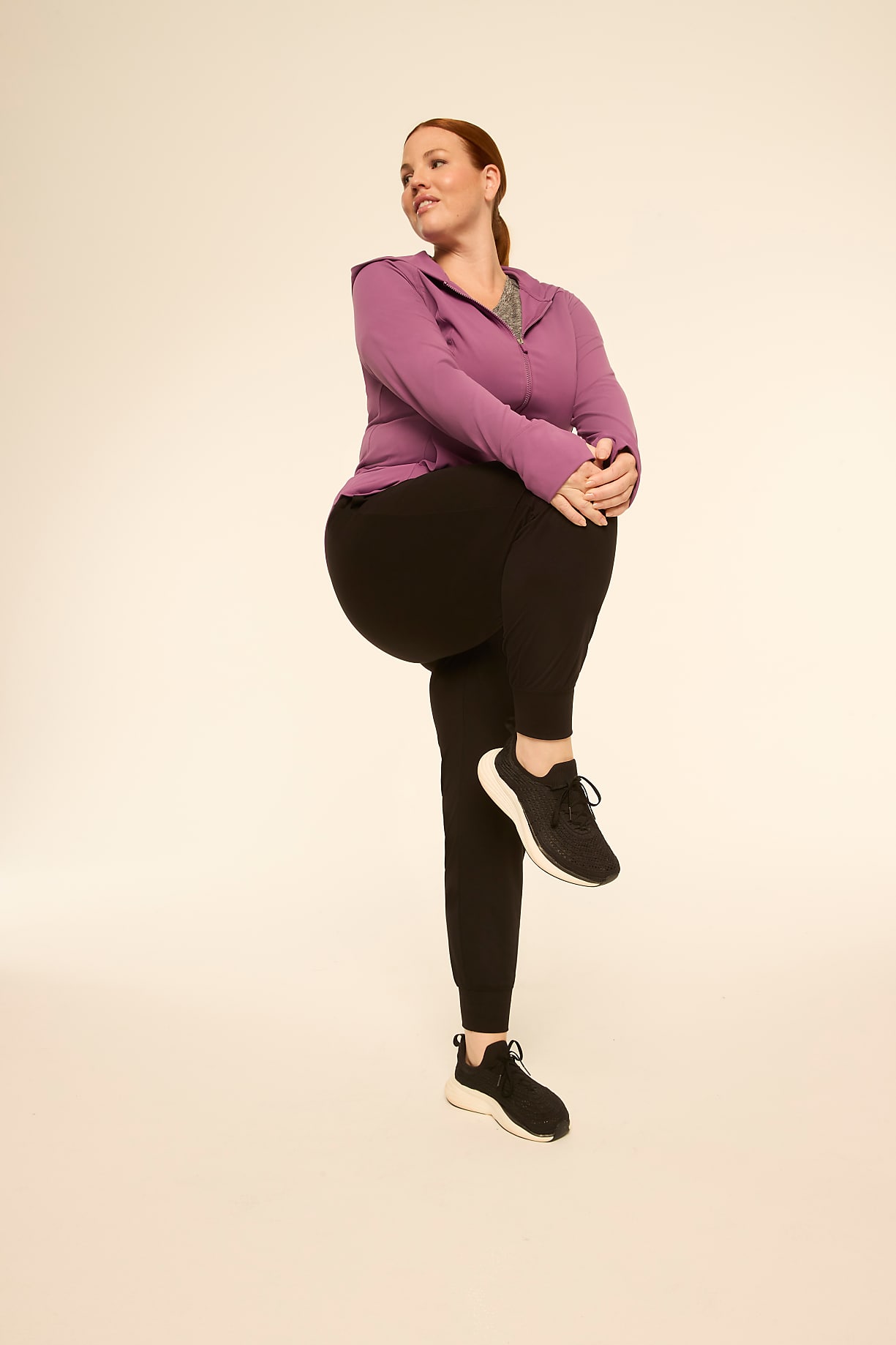 A woman in athletic wear stretches her leg in the foreground against a plain, light-colored background. Product Image 5