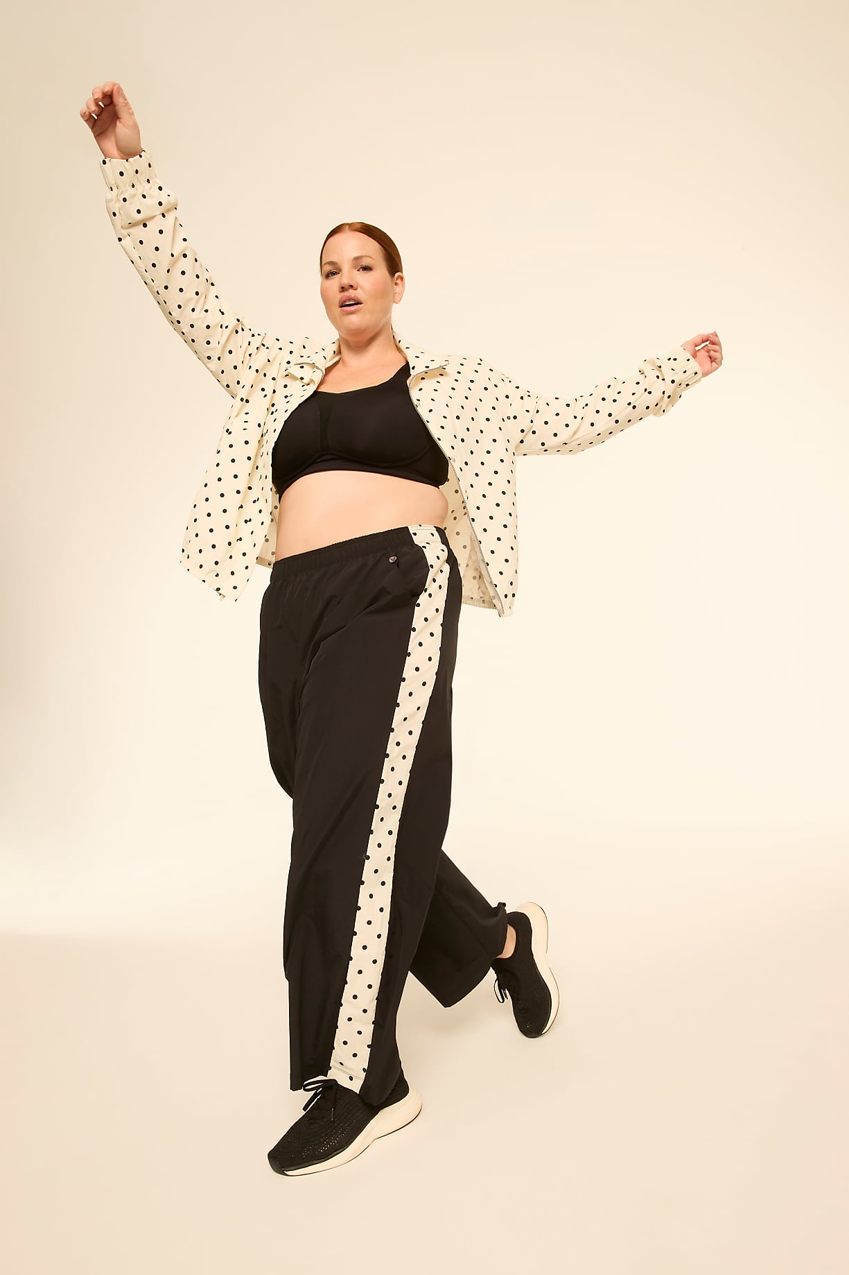 A woman in a polka-dot shirt and track pants with a polka-dot stripe poses against a plain, light-colored background. Product Image 11