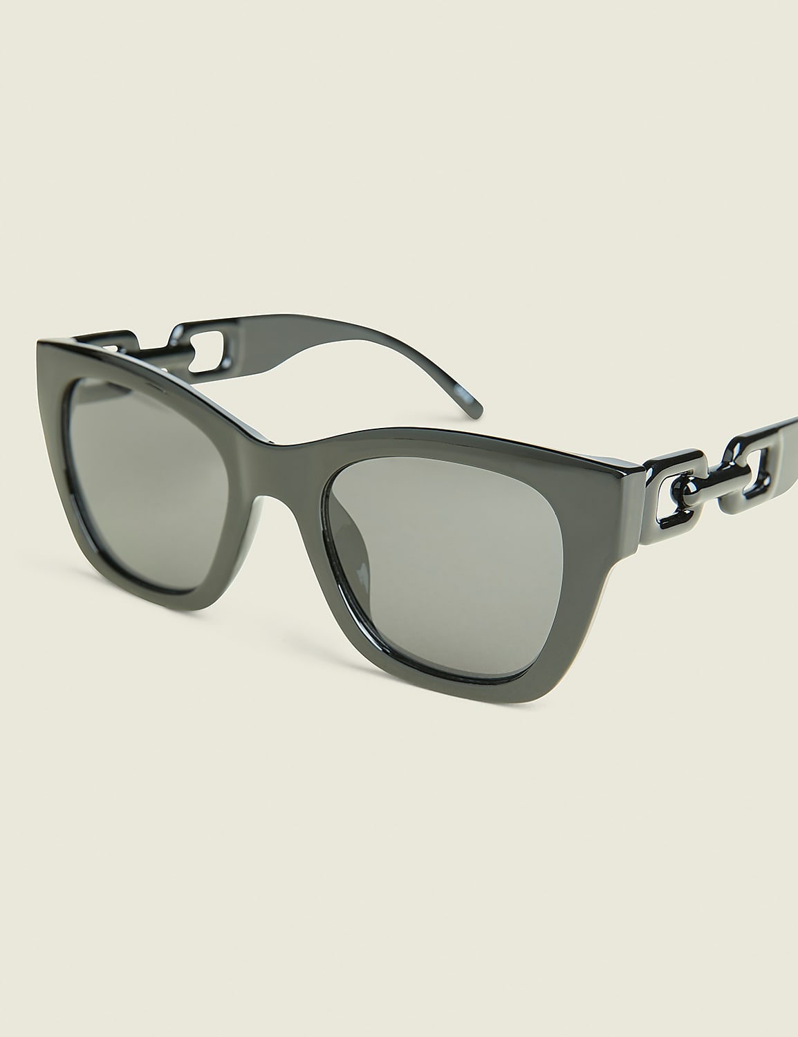 A pair of dark, stylish sunglasses with chain detailing on the arms rests against a plain, light-colored background. Product Image 1