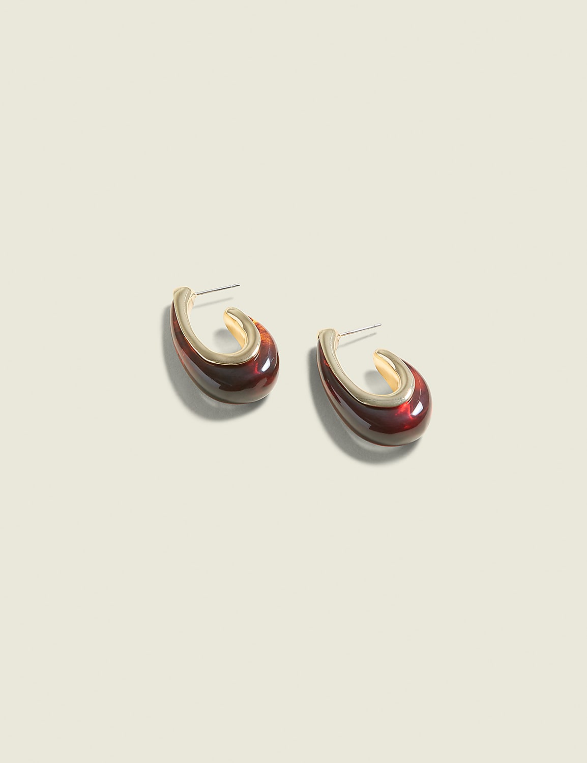 A pair of dark red, gold-rimmed hoop earrings rests on a pale, textured background. Product Image 1