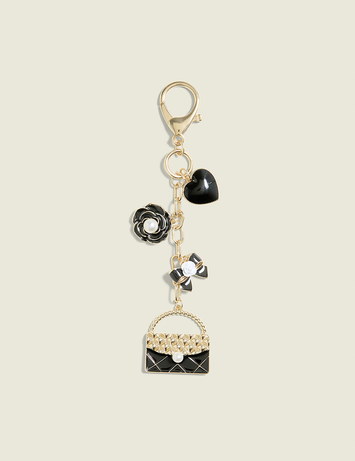A gold keychain with charms of a black quilted handbag, a white and black bow, a black rose with a pearl, and a black heart hangs against a plain cream background. Product Image 1