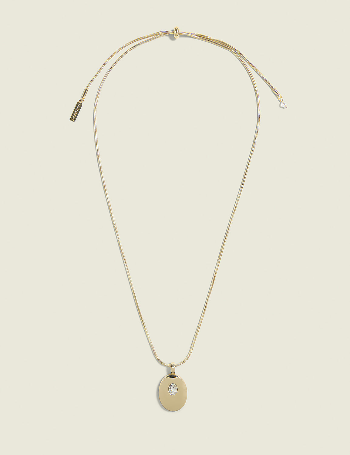 A delicate gold necklace with a circular pendant featuring a small inset gem hangs against a plain, light beige background. Product Image 1