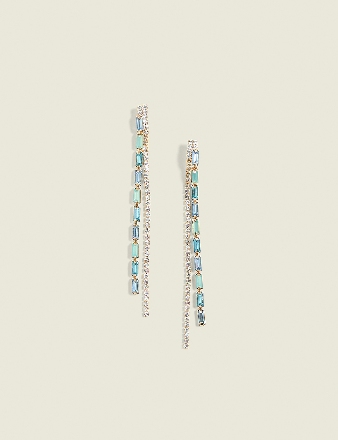 Two delicate gold drop earrings with alternating clear and blue gemstones hang against a soft, pale yellow background. Product Image 1