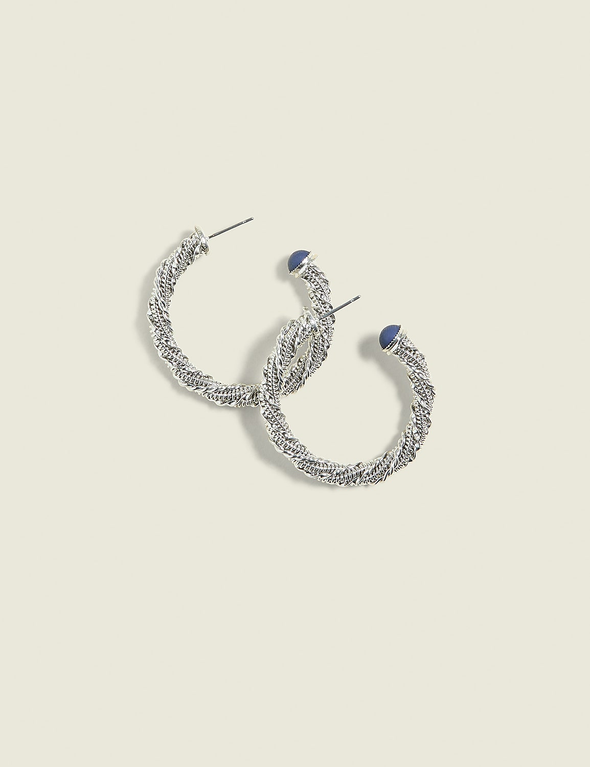A pair of silver twisted hoop earrings with small blue stones rests on a pale yellow background. Product Image 1