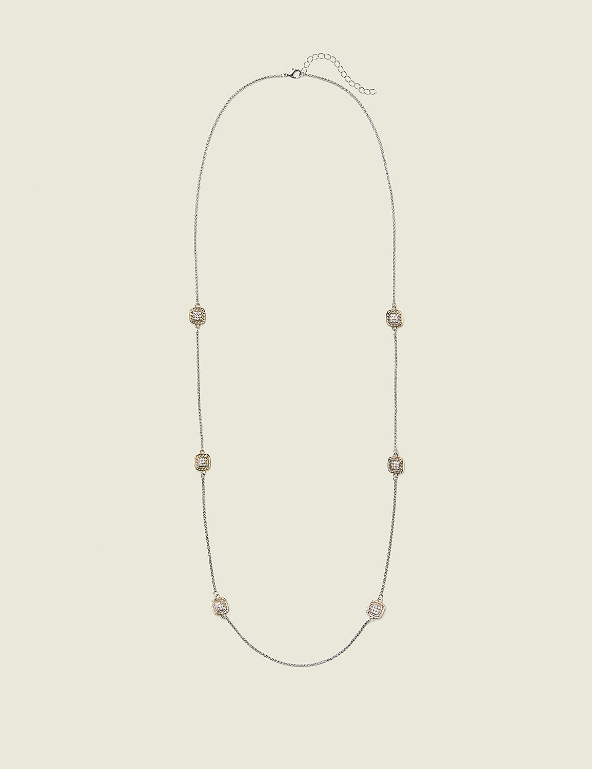 A long, delicate silver chain necklace with seven square, rose-gold toned charms is laid out against a plain, light beige background. Product Image 1