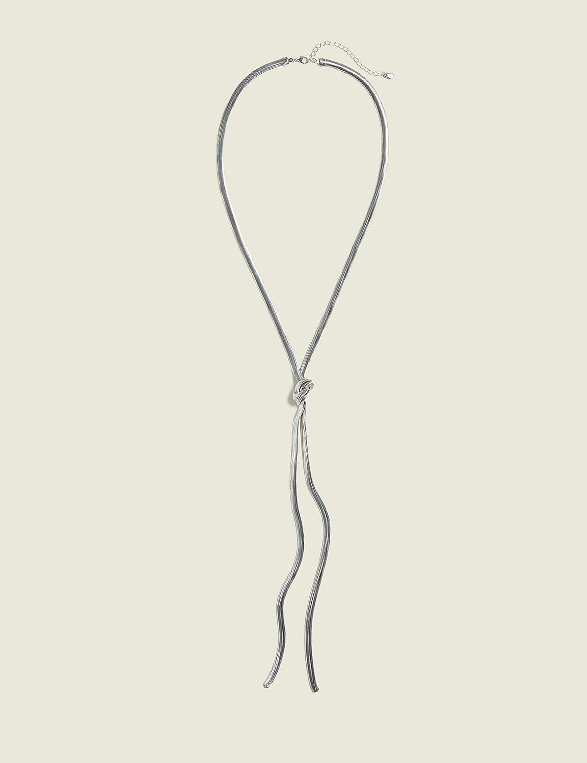 A silver knot necklace with dangling chains rests against a plain, light beige background. Product Image 1