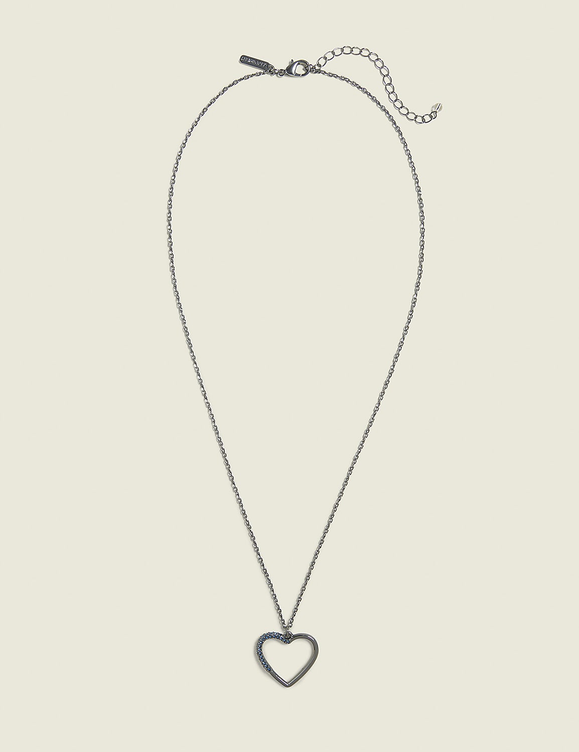 A silver heart pendant hangs from a delicate chain against a plain, light beige background. Product Image 1