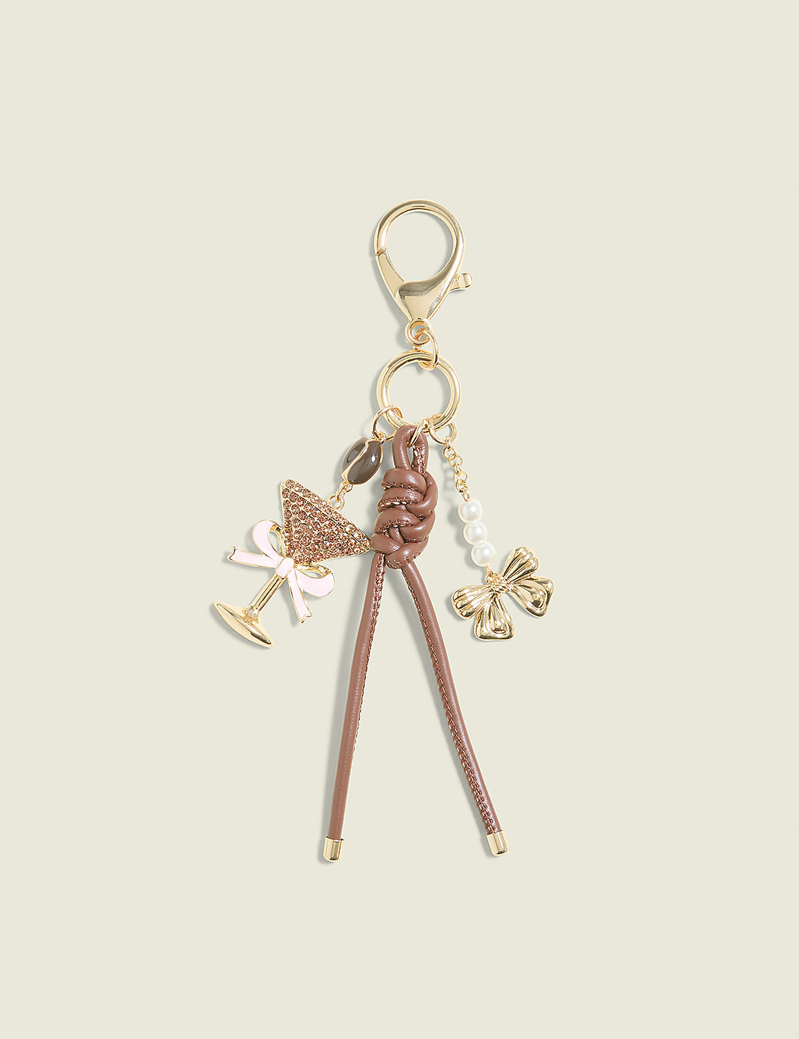A brown leather braided keychain with charms of a martini glass, a bow, and pearls hangs against a plain cream background. Product Image 1