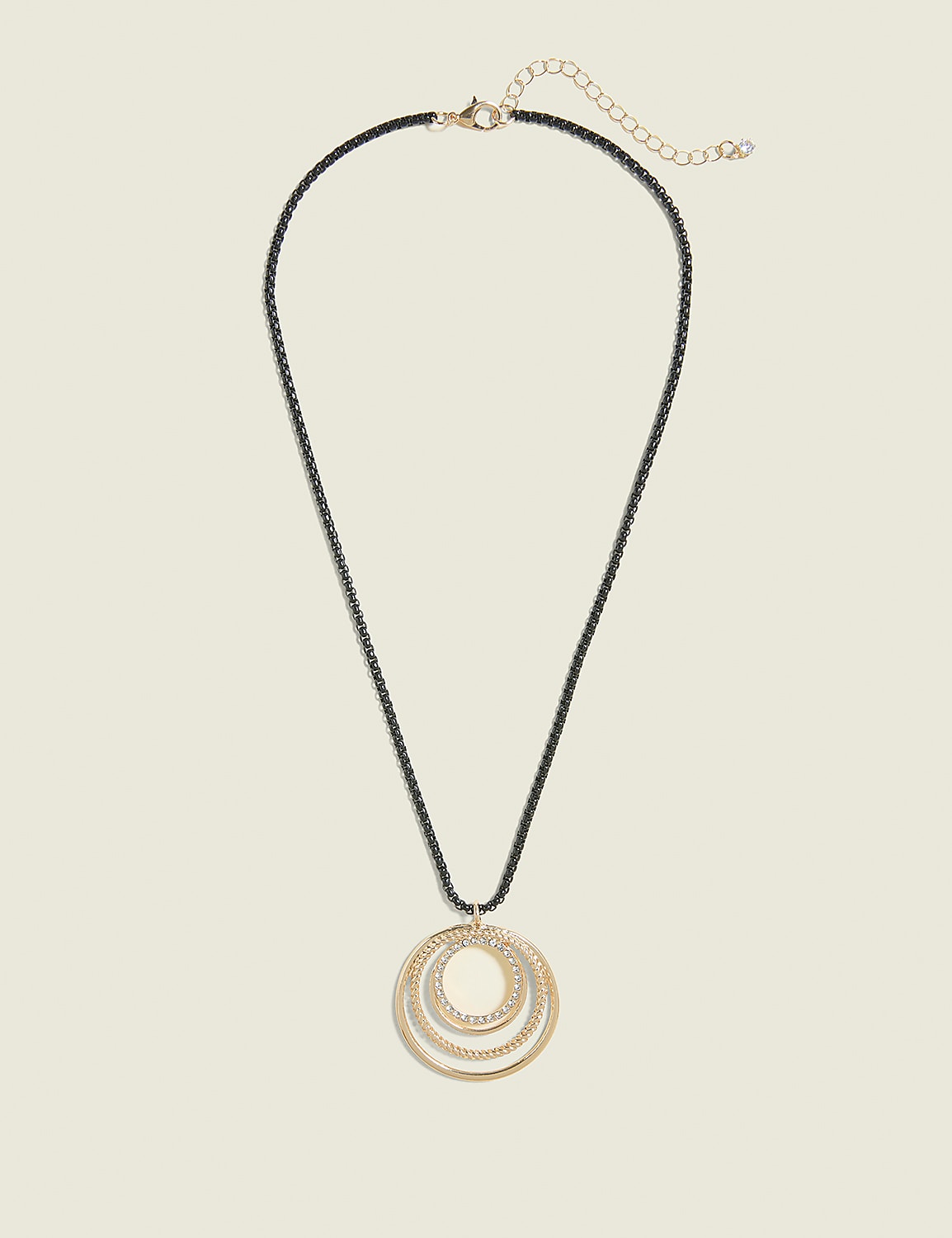 A gold pendant with three nested, sparkling rings hangs from a dark chain against a plain, light beige background. Product Image 1