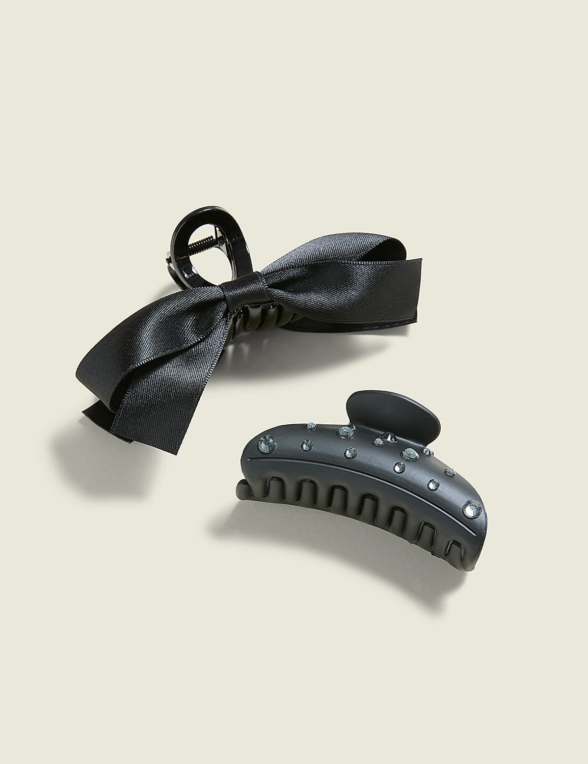 Two black hair clips, one with a satin bow and the other adorned with rhinestones, rest on a plain, light-colored background. Product Image 1