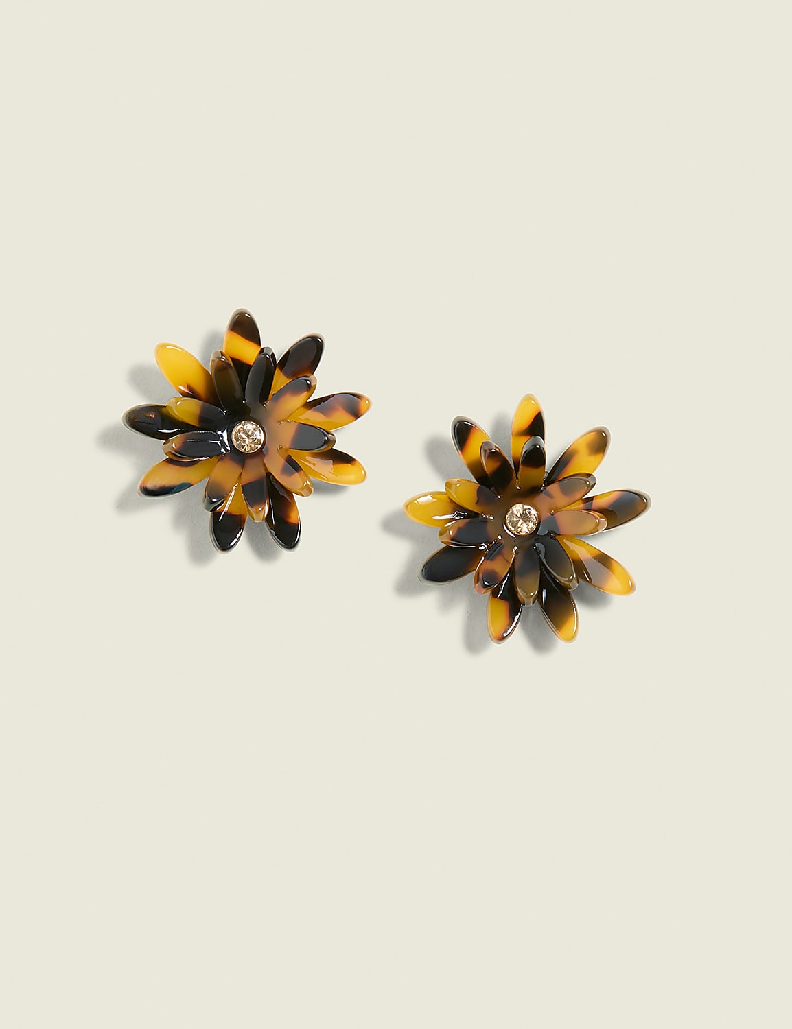 Two tortoise-shell flower-shaped earrings with a small gem in the center rest on a pale green background. Product Image 1