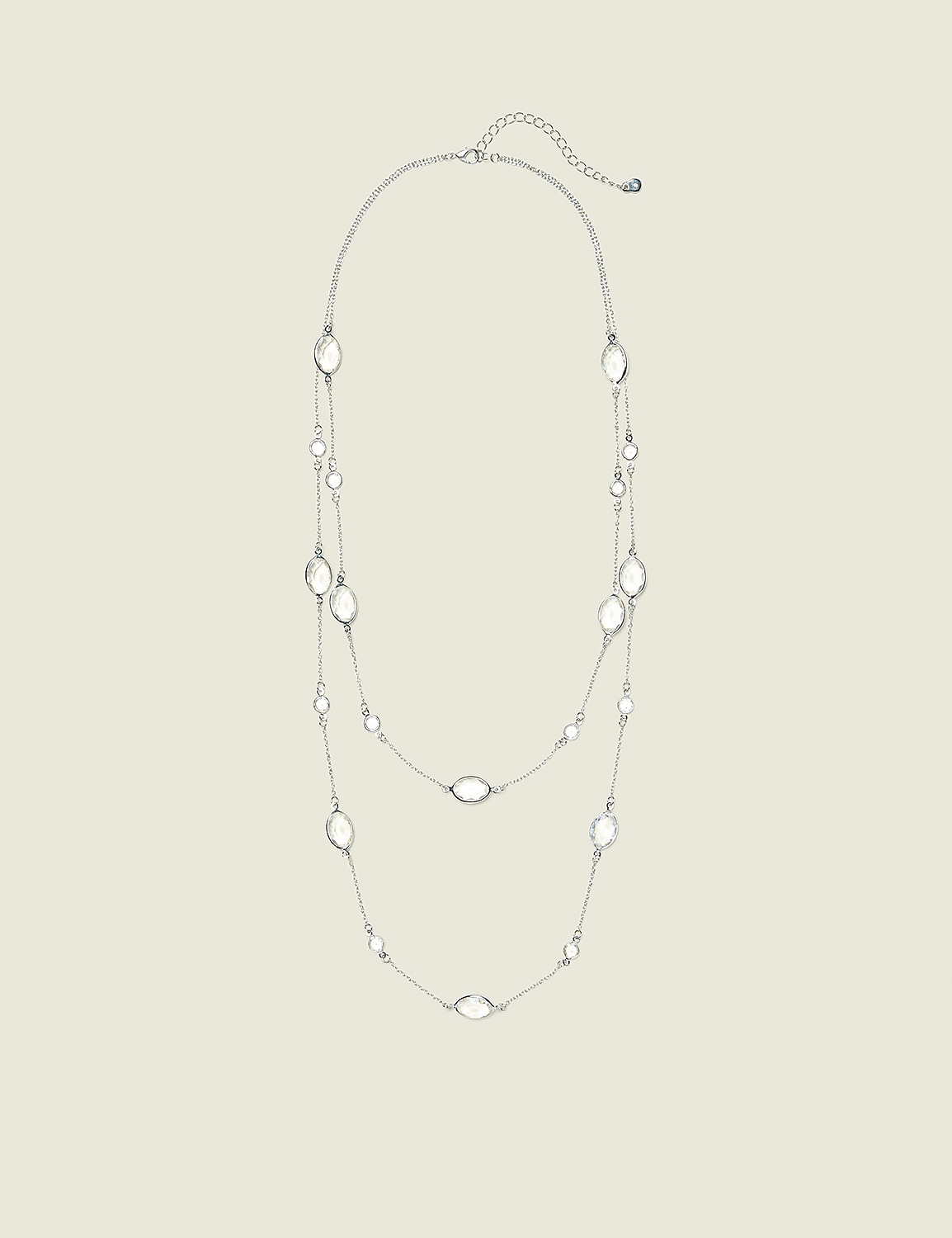 A delicate silver necklace with clear oval-shaped pendants is displayed against a plain, light beige background. Product Image 1