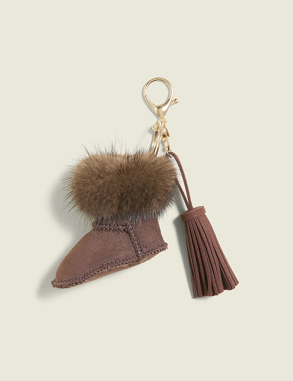 A fuzzy brown boot keychain with a tassel hangs against a plain, light brown background. Product Image 1