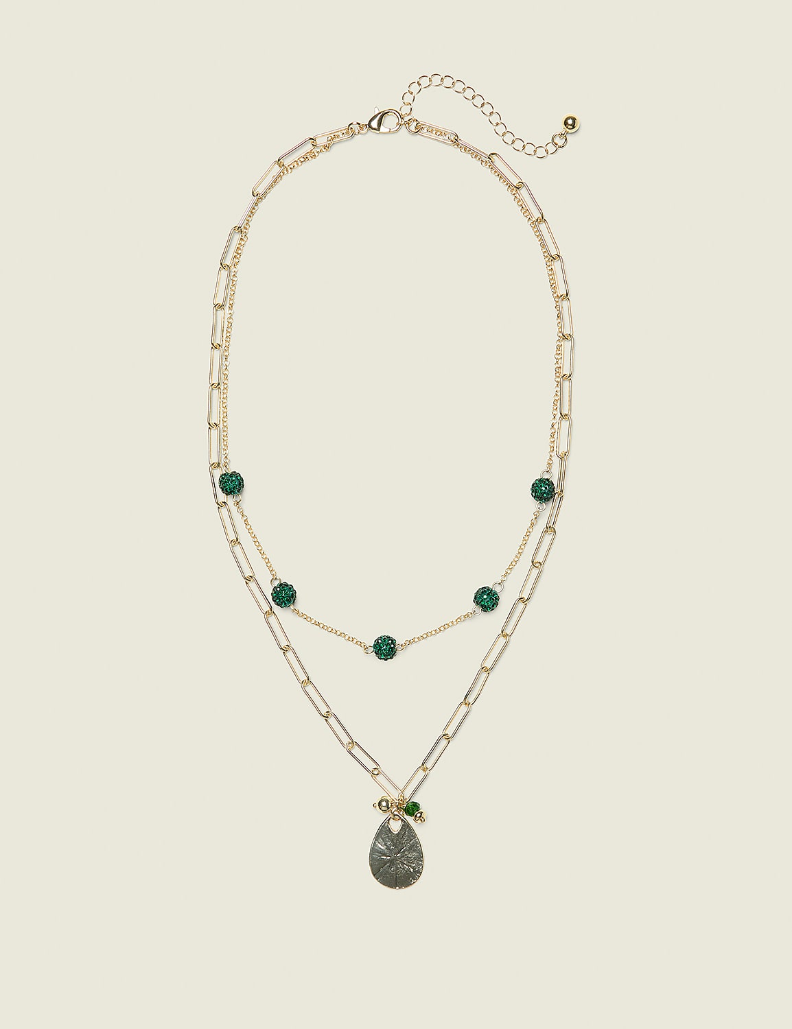 A layered gold necklace with green beads and a pendant hangs against a plain, light beige background. Product Image 1