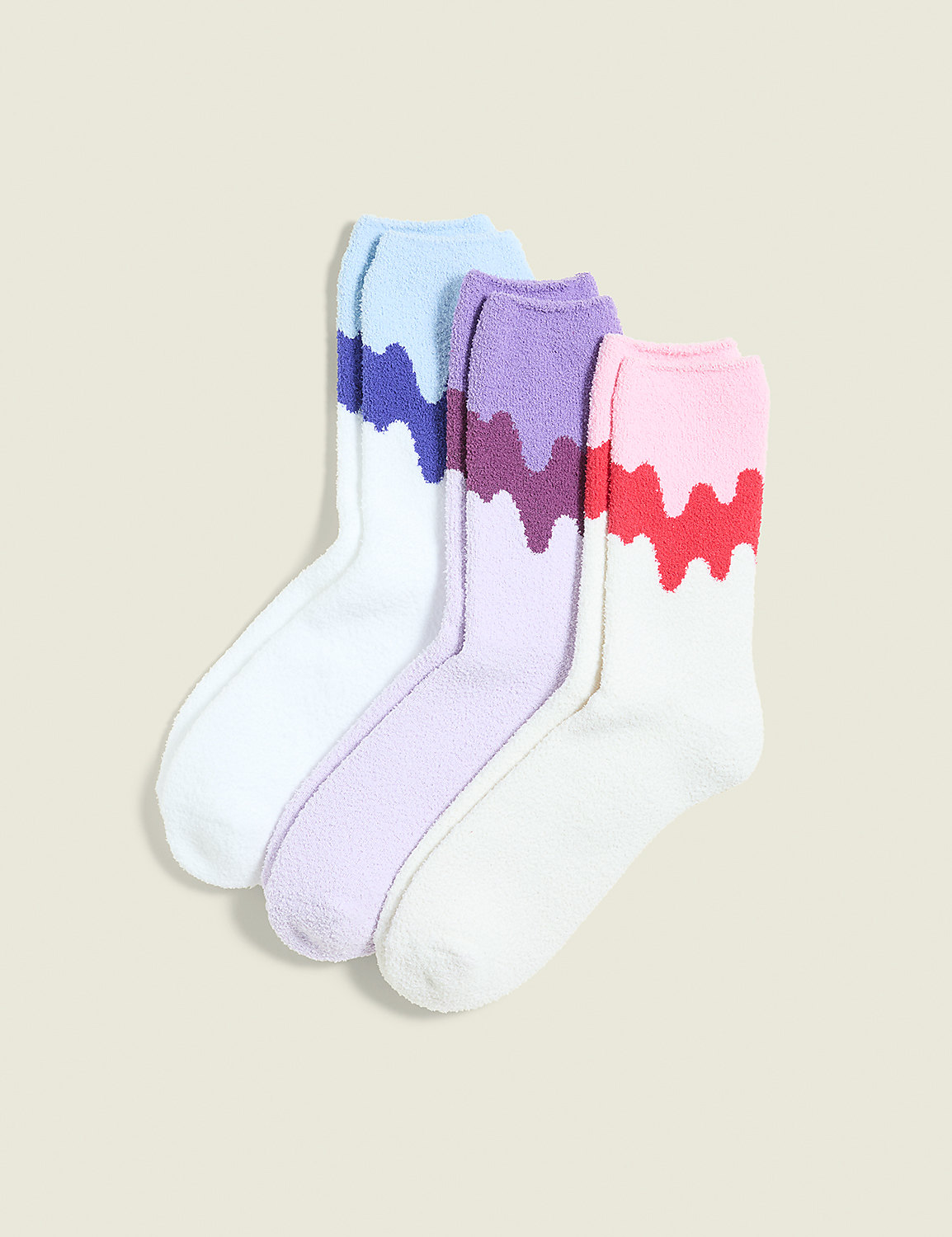 Three pairs of fluffy socks with colorful, dripping patterns are arranged in the foreground against a plain, light-colored background. Product Image 1