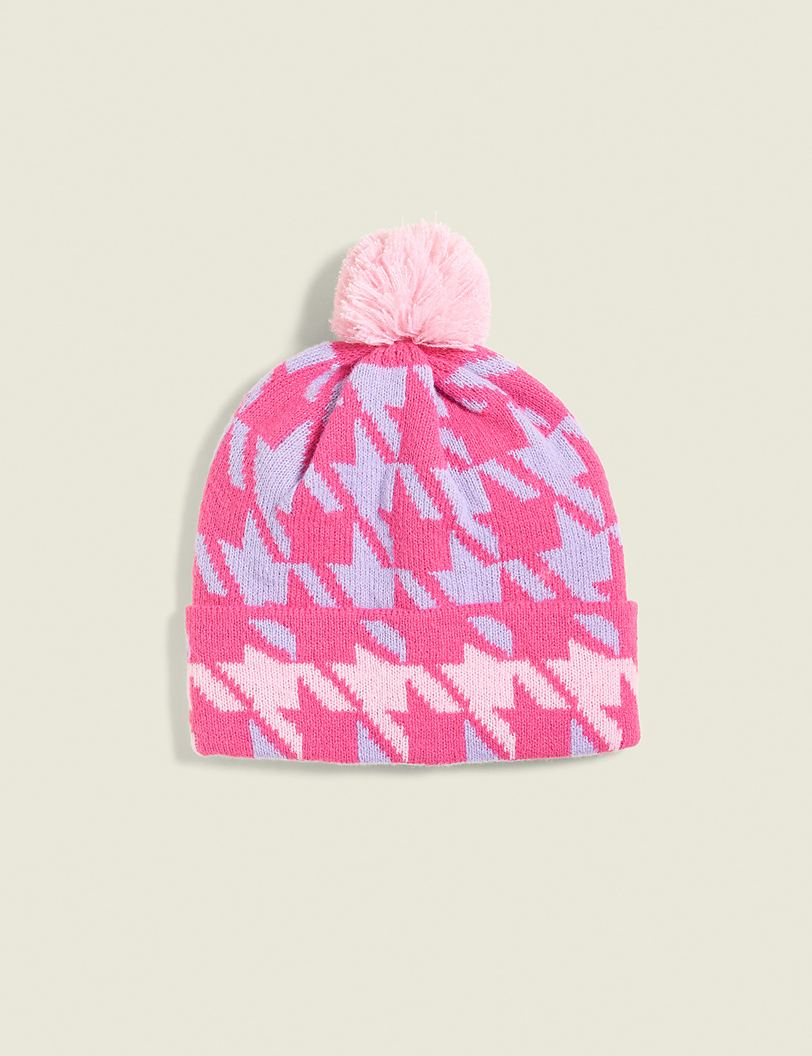 A pink and purple houndstooth knit beanie with a light pink pom-pom sits against a pale green background. Product Image 1
