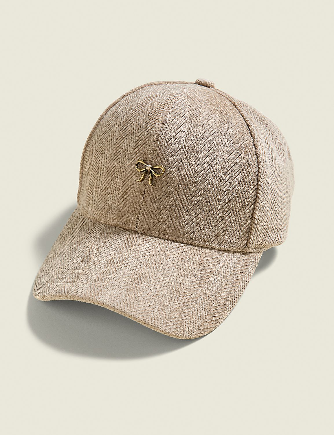 A beige herringbone baseball cap with a small gold bow accent sits on a plain, light beige background. Product Image 1