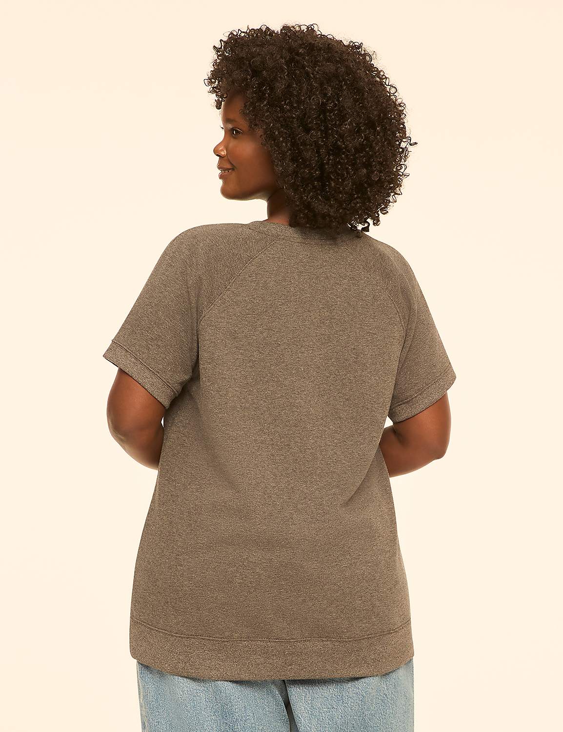 A woman with curly dark hair, wearing a gray t-shirt and blue jeans, stands against a plain cream background. Product Image 2