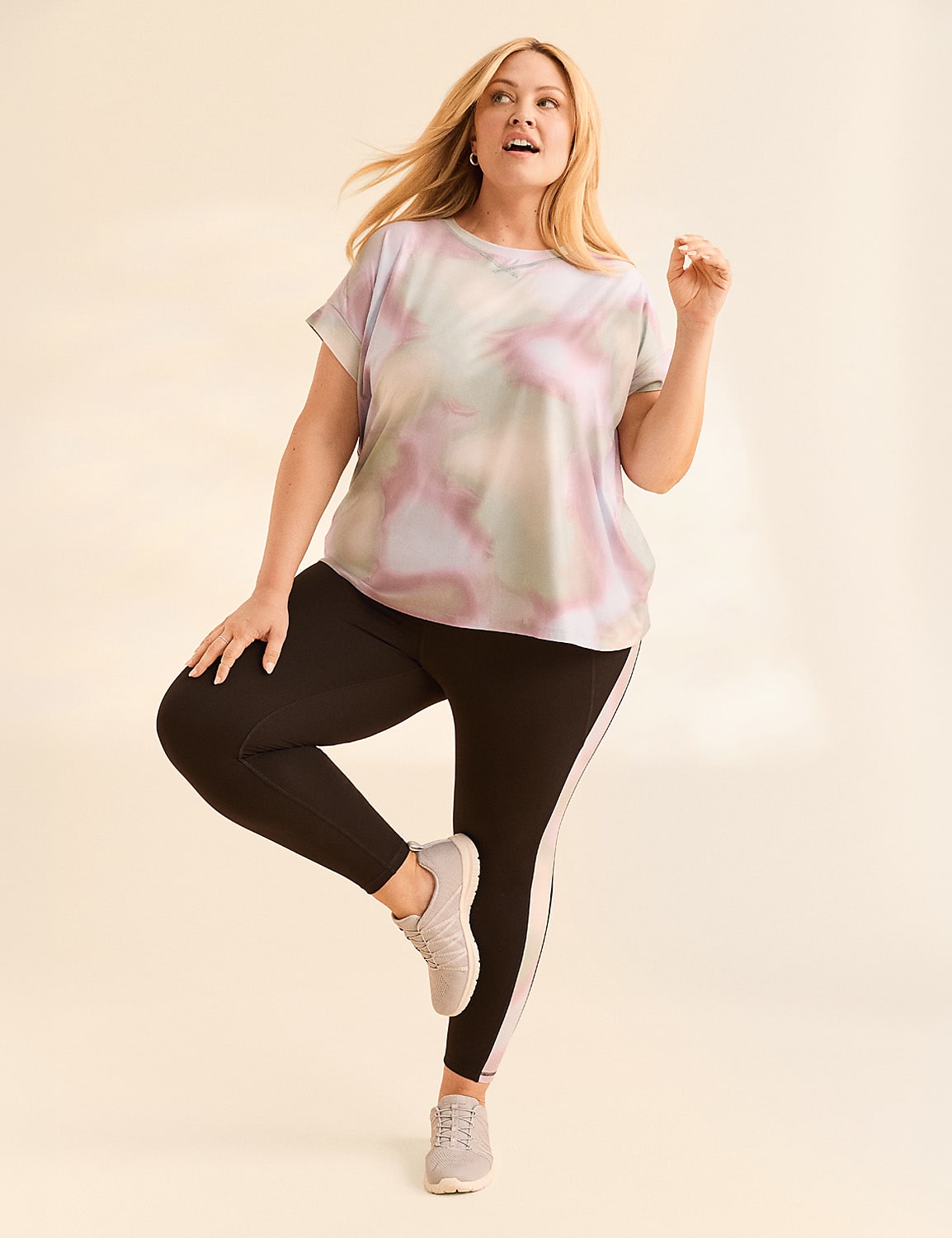 A woman in a tie-dye shirt and black leggings stands on one leg against a plain, light-colored background. Product Image 4
