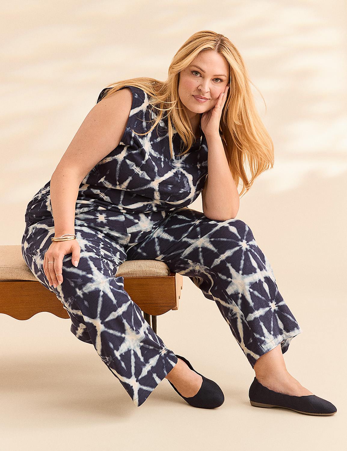 A woman in a tie-dye jumpsuit sits on a bench against a soft, textured background. Product Image 4