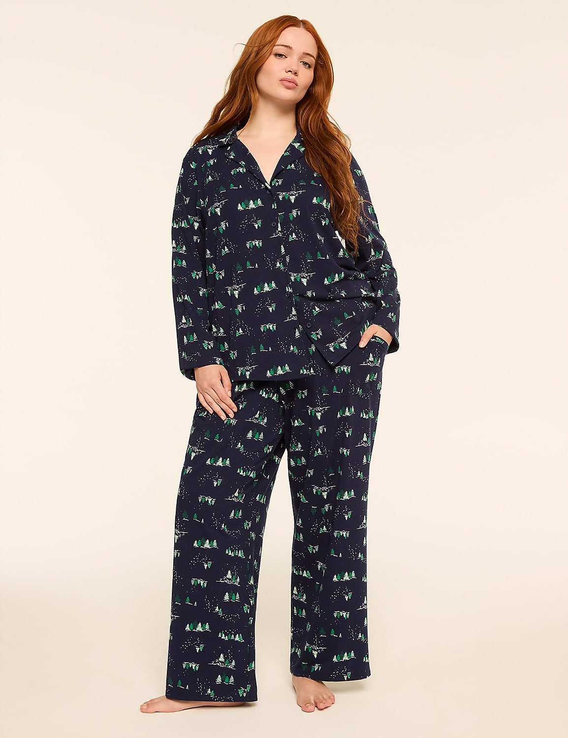 A woman with long red hair stands in a dark blue pajama set with a forest print, against a plain cream background. Product Image 1