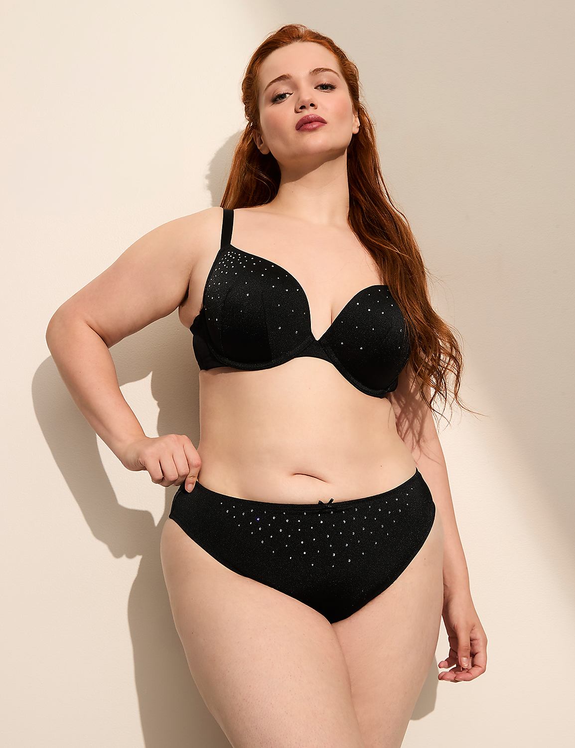 A woman with red hair poses in black lingerie against a plain, light-colored wall with soft shadows. Product Image 4